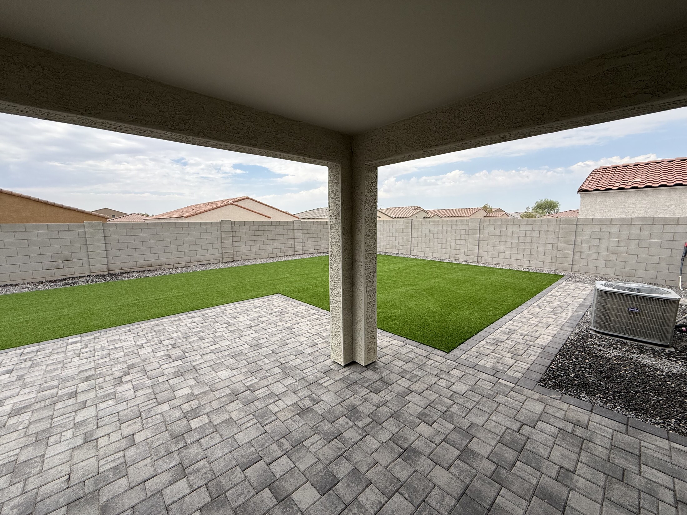 Covered paver patio opening onto a backyard turf area
