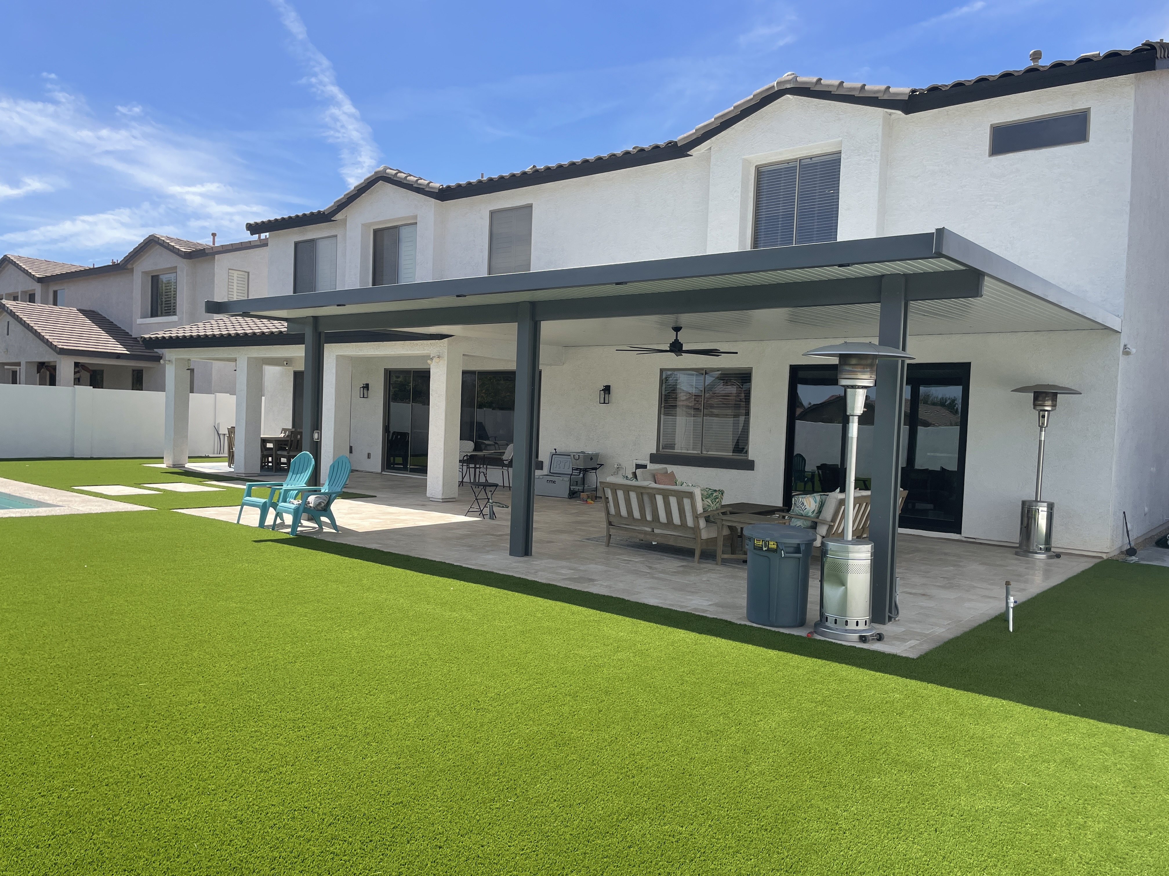 Covered patio and artificial turf installation behind a two-story home