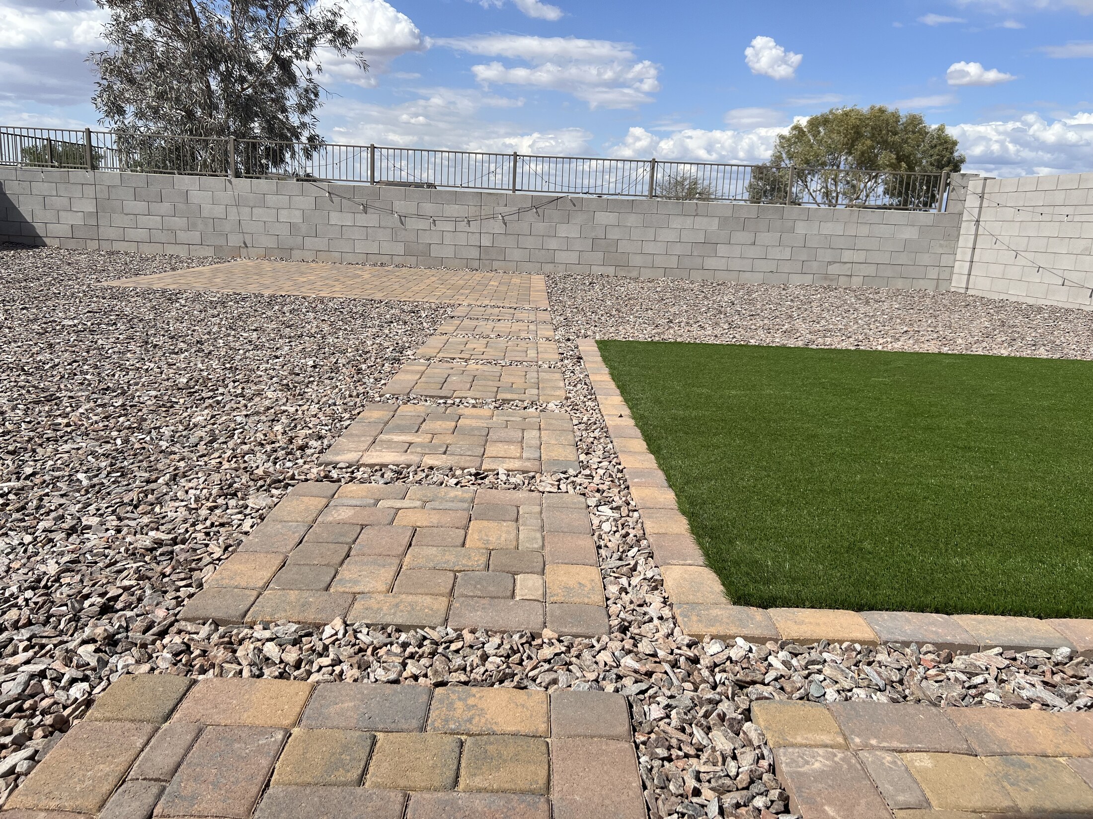 Paver stepping path through a gravel yard beside a turf square