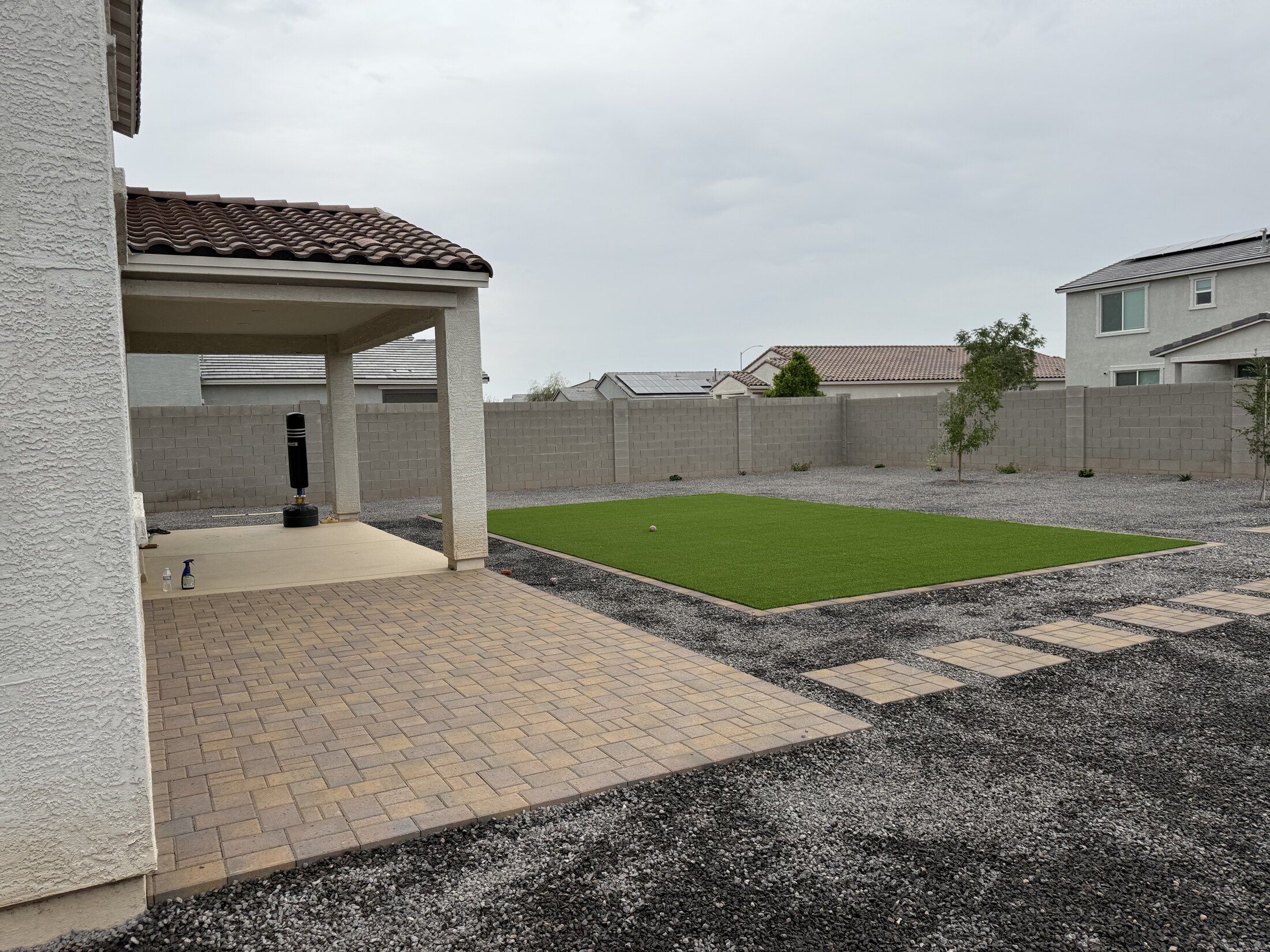 Covered patio with pavers, gravel yard, and turf accent